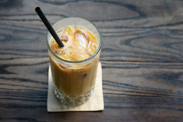 A close-up of an iced latte served in a glass with ice cubes and a straw, placed on a wooden table, highlighting its refreshing and creamy texture