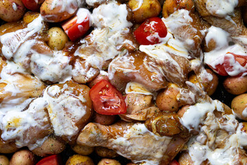 Baked chicken leg quarters seasoned with garlic and herbs with potatoes in a baking dish on a wooden table close up view