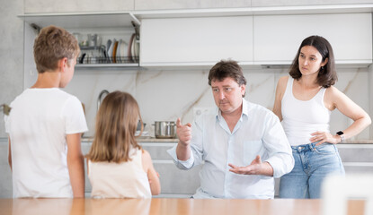 Fototapeta premium Mom and dad scold their guilty daughter and son in kitchen at home