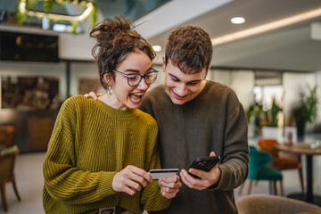 cheerful young couple use credit card for online shopping on cellphone
