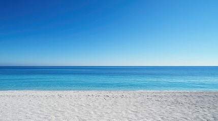 Fototapeta premium A wide expanse of untouched beach sand leading to a calm blue sea under clear skies.