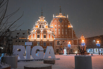 The House of the Blackheads in Riga, Latvia, glows with warm lights. Snowfall, blue lit trees, and...