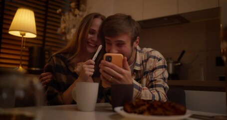 Happy guy in a plaid shirt hugging his girlfriend and talking on the phone showing a pregnancy test during a happy evening at home - Powered by Adobe