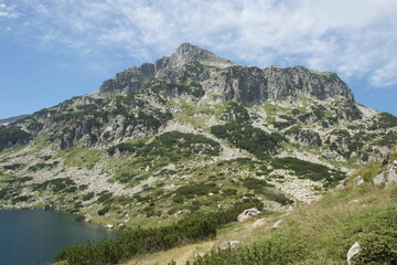 Mountain peak, rocky slopes, lush greenery. Lake reflects clear blue sky. BULGARIA. Nature's...