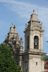 Soaring church towers adorned with intricate details and a bell pierce the clear blue sky in Braga,...