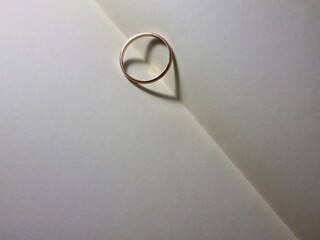 Background with golden ring and heart shaped shadow on open blank notebook pages
