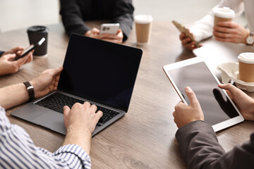 Group of people using different gadgets at wooden table in office, closeup. Modern technology