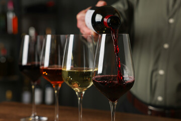 Professional sommelier pouring red wine into glasses on wooden table indoors, closeup