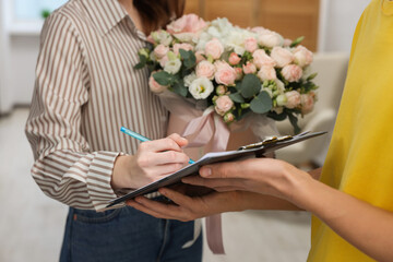 Woman signing for delivered gift box with floral composition indoors, closeup