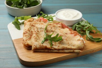 Delicious crepes with salmon, cream cheese and arugula on blue wooden table, closeup