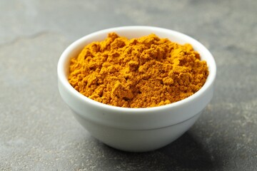 Turmeric powder in bowl on grey table, closeup