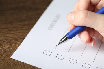 Woman checking box of paper form at wooden table, closeup