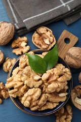 Fresh walnuts and green leaves in bowl on blue wooden table, flat lay