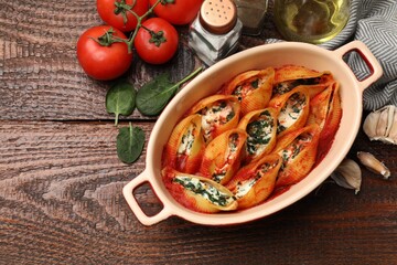 Delicious conchiglie pasta with ricotta cheese, spinach and tomato sauce in baking dish on wooden table, flat lay. Space for text