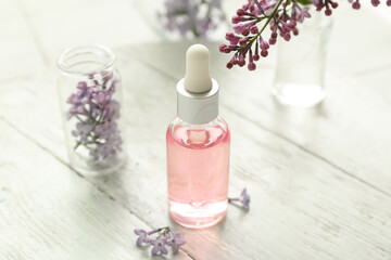 Bottles of cosmetic oil with beautiful lilac flowers on white table