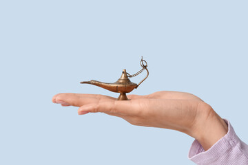 Young Muslim woman with Aladdin lamp on blue background, closeup. Islamic New Year celebration