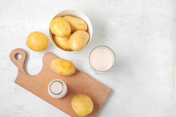 Bottle and glass of tasty potato milk with fresh vegetables on light background
