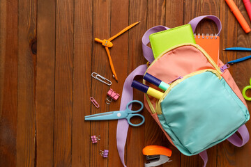 Colorful school backpack with different stationery on wooden background