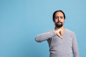 Young dissatisfied person showing thumbs down symbol in studio, expressing his denial and rejection...