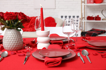 Festive table setting decorated for Valentine's Day with red roses and burning candles at home
