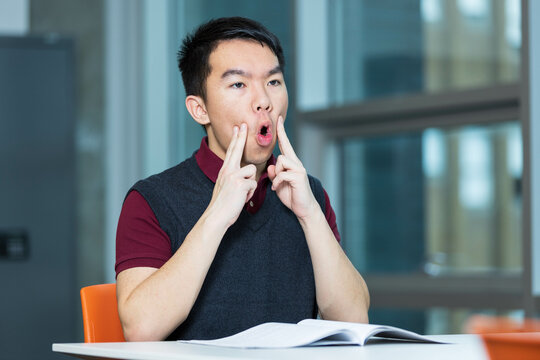 A young teenage boy is doing oral motor exercises in a room. He could be doing singing practice, vocal training, or speech therapy, improving articulation, enunciation and reducing speech impediments