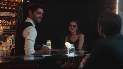 Focusing on beautiful woman guest sitting in special drink gin fizz at luxurious counter bar at vibrant nightlife party atmosphere. Smart bartender wiping glass while talking with customer. Vinosity.