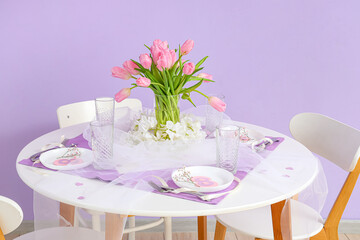 Dining table with setting and tulip flowers served for International Women's Day celebration near color wall in room