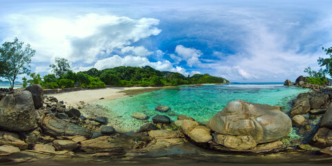 Crystal-clear waters surround smooth rocks on a small beach, with a backdrop of greenery under a bright sky. Port Glaud Lagoon. Seychelles. VR 360.