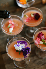 Colorful floral cocktails being prepared on a rustic wooden table for a celebration event during daytime hours