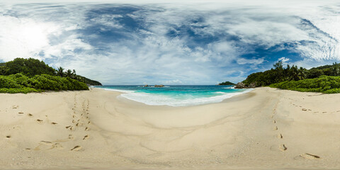 Golden sands stretch out with footprints leading toward turquoise waves, bordered by lush tropical greenery. Anse Petit Boileau, Seychelles. Monoscopic image.