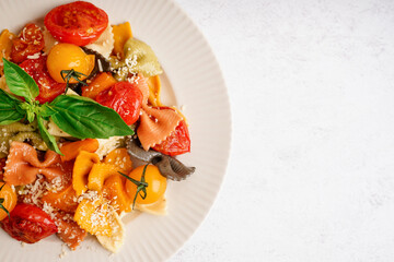 Plate of delicious farfalle pasta with tomato and basil on white background