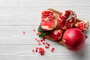 Board with fresh ripe pomegranates and seeds on white wooden background