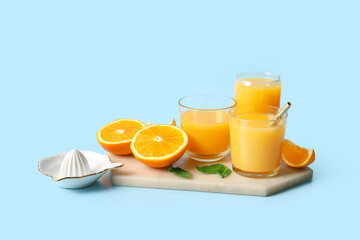 Glasses of fresh orange juice with mint and juicer on blue background