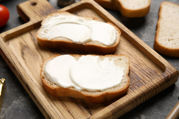 Cutting board of tasty bruschetta with processed cheese on black background. Closeup