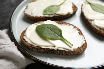 Plate of tasty bruschetta with processed cheese and spinach leaves on black background. Closeup