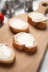 Cutting board of tasty bruschetta with processed cheese on white wooden background, closeup