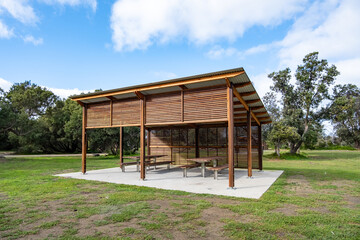 A modern park shelter with timber battens and slatted walls on a concrete platform, provides a...