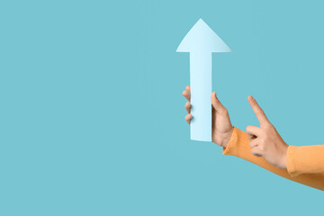 Female hands with paper arrow pointing at something on blue background