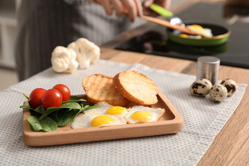 Woman preparing tasty dinner with fried quail eggs, fresh vegetables and toasts in kitchen, closeup