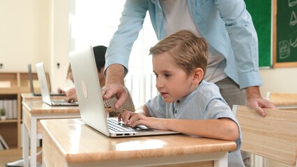 Caucasian teacher helping energetic boy coding engineering prompt while diverse student using...