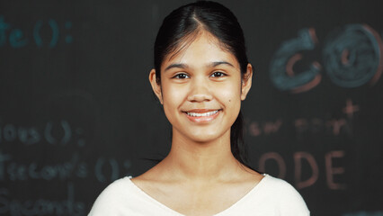 Caucasian woman looking at camera while standing at blackboard. Cute happy student smiling while...