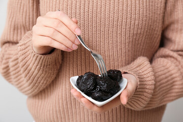 Woman holding bowl with dried prunes and fork on grey background, closeup