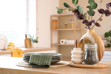 Vase with eucalyptus branches, dishes and napkin on table in kitchen