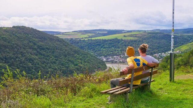 Couple with arms around sitting on bench taking in scenic nature view of the Rhine River Valley, Oberwesel, Germany