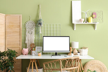 Stylish workspace with modern computer and folding screen near green wall