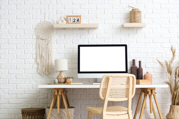 Stylish workspace with modern computer and pampas grass near white brick wall
