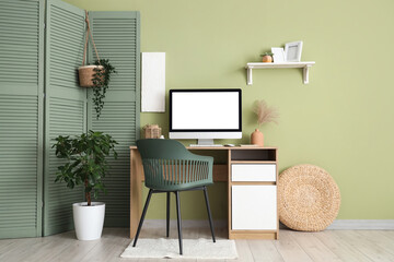 Stylish workspace with modern computer and folding screen near green wall