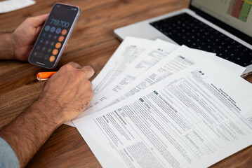 Man working on tax documents with calculator and laptop on wooden table. Financial analysis and tax preparation concept 