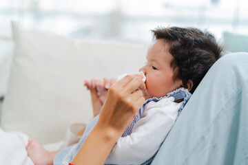 Mother cleaning baby's nose with soft tissue, affection and care in a bright setting