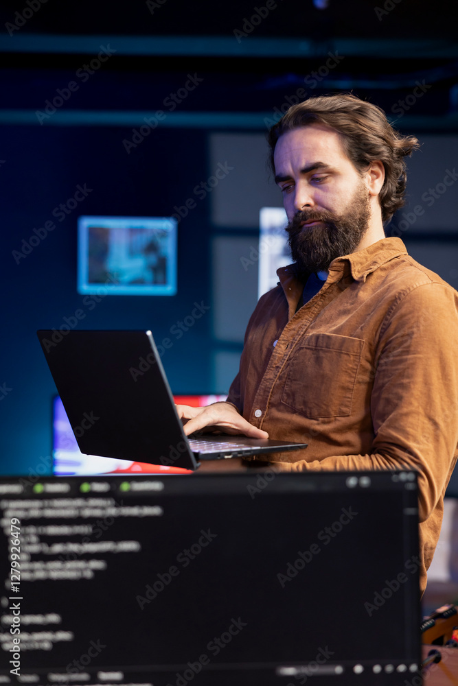 Poster computer scientist walking in apartment designing and developing software applications using laptop.